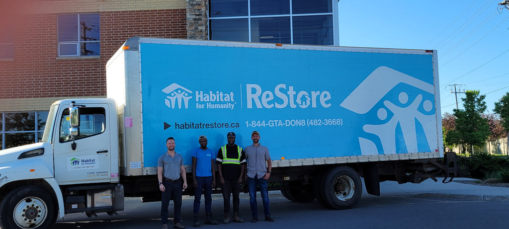 Staff standing, smiling beside large blue truck that says ReStore