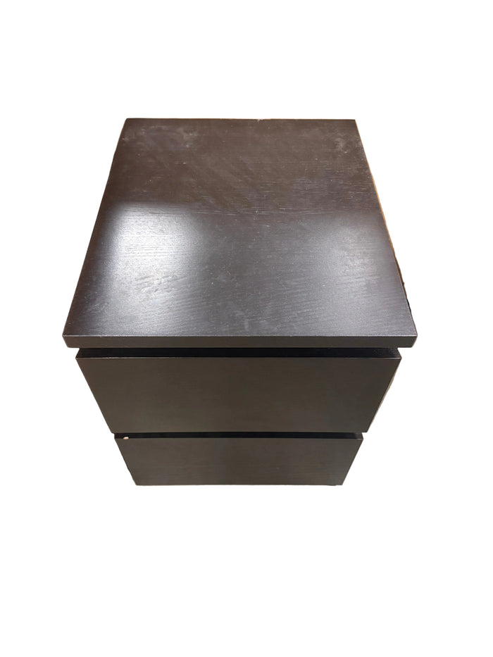 A dark brown wooden two-drawer nightstand or storage cabinet, photographed from a top-down angle in what appears to be a warehouse or showroom setting.