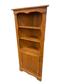 A wooden three-compartment bookcase with a single door, photographed in a warehouse or furniture showroom setting.