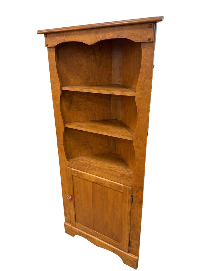 A wooden three-compartment bookcase with a single door, photographed in a warehouse or furniture showroom setting.