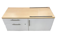 A white office storage cabinet with a light wood top, featuring two drawers on the left and a single door on the right, with silver metal handles.