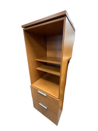 A mid-century modern wooden cabinet with a warm medium-brown finish, featuring open shelving on the left and a lower cabinet section with two drawers on the right, photographed in a warehouse setting.