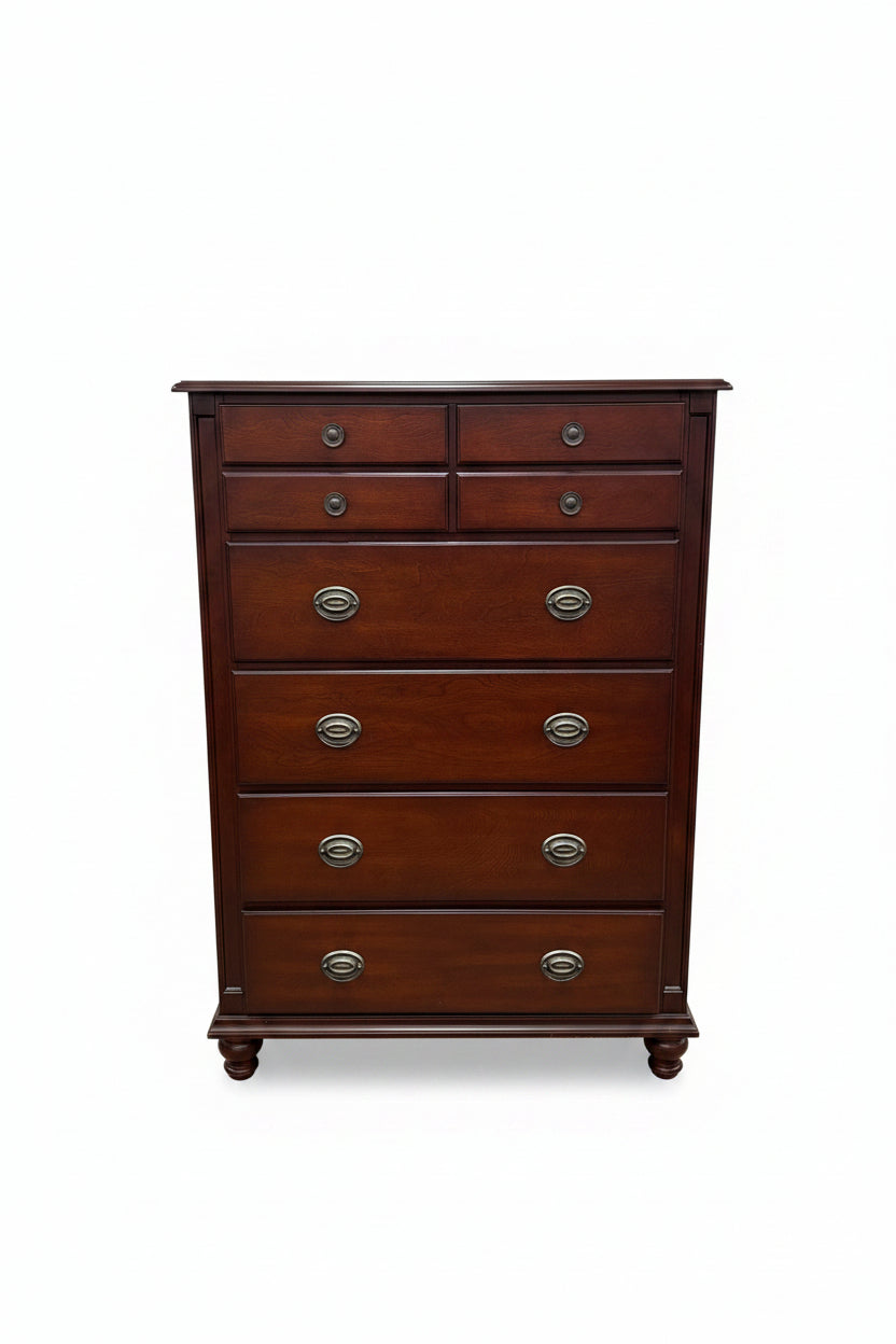 A dark reddish-brown wooden chest of drawers with six drawers and round metal pulls, photographed in a furniture store showroom.