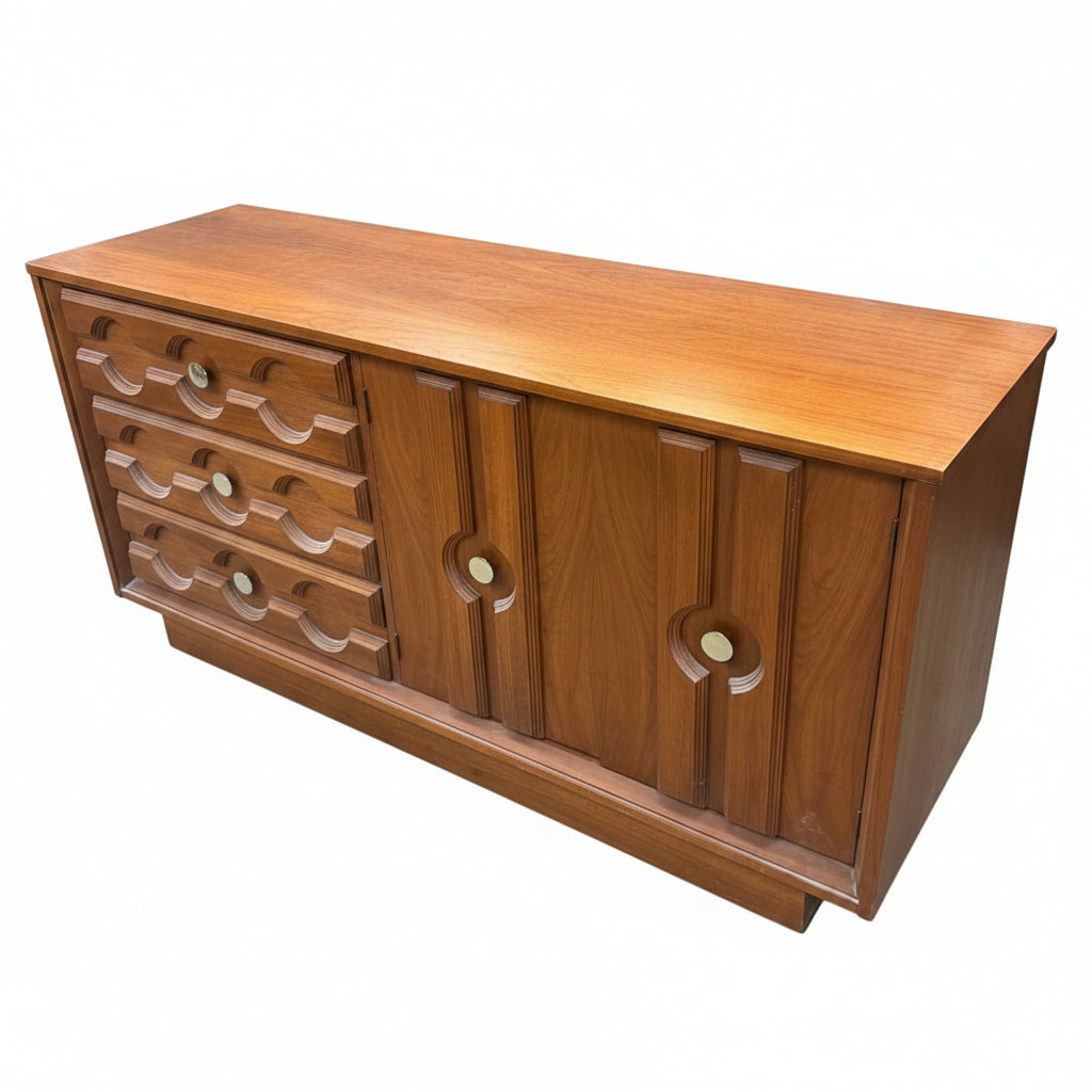 A mid-century wooden sideboard or credenza with a warm medium-brown finish, featuring a row of curved drawer pulls on the left and two cabinet doors with circular cutouts on the right, photographed in a furniture store.