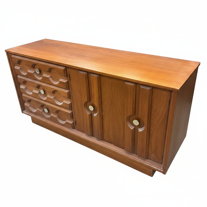 A mid-century wooden sideboard or credenza with a warm medium-brown finish, featuring a row of curved drawer pulls on the left and two cabinet doors with circular cutouts on the right, photographed in a furniture store.