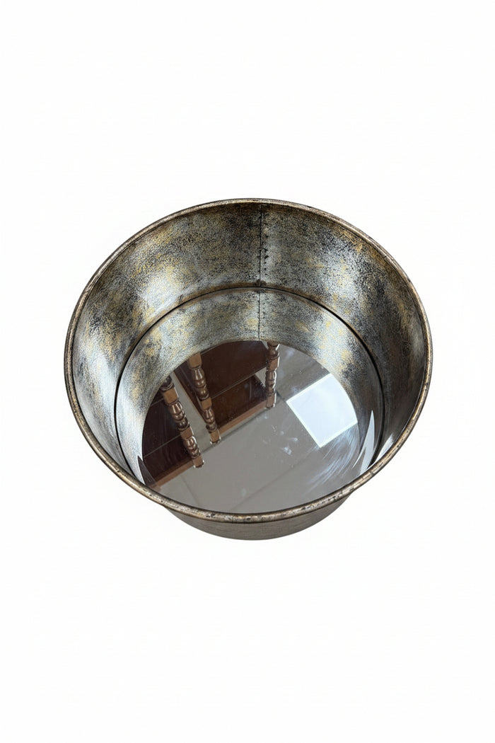 A large oval metal tub with a distressed silver and gold finish, displayed on a wooden side table in a home setting.