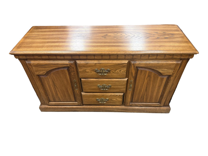 A medium brown wooden sideboard or credenza with three drawers in the center and two arched cabinet doors on the sides, shown in what appears to be a furniture store or warehouse.
