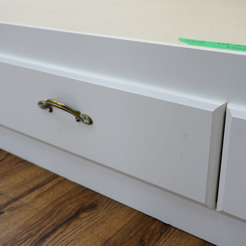 Close-up of a white drawer with a gold handle on a wooden floor.