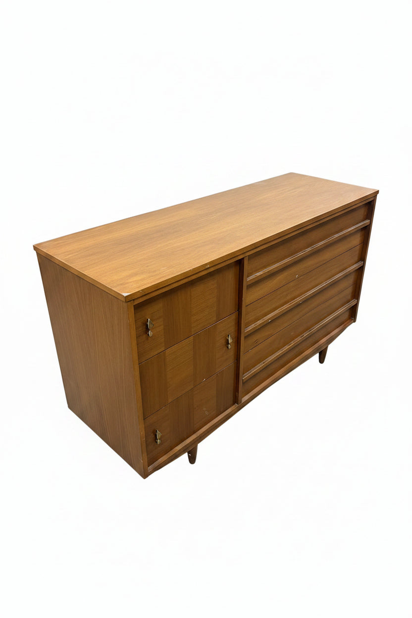 A mid-century modern wooden dresser with a warm medium-brown finish, featuring a cabinet on the left and multiple drawers on the right, photographed in a furniture showroom.