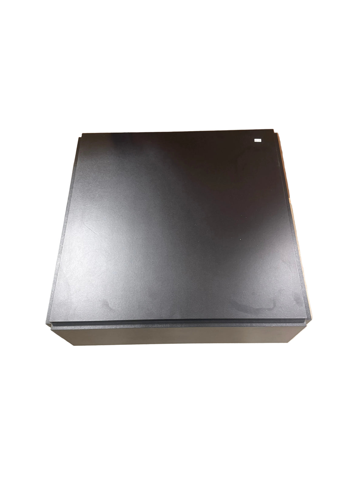 A black rectangular metal box or cabinet with a matte finish, photographed from above on a concrete floor next to wooden panels.